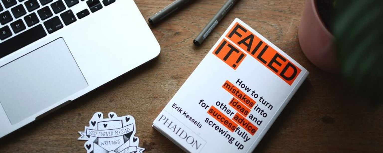 Buch mit dem Titel Failed IT auf einem Schreibtisch mit Laptop